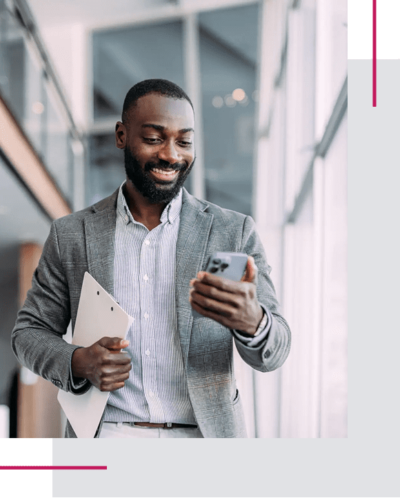 A smiling man in a suit checking his phone indoors.