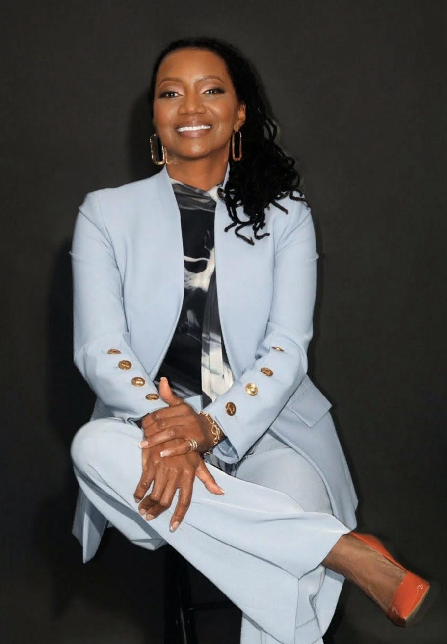 Confident woman in a stylish light blue suit sitting gracefully against a black background.