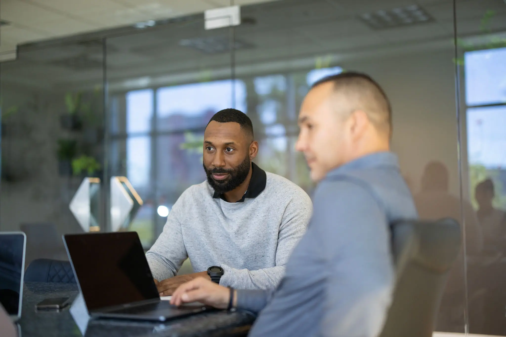 Two men engaged in a discussion with a laptop in an office setting.