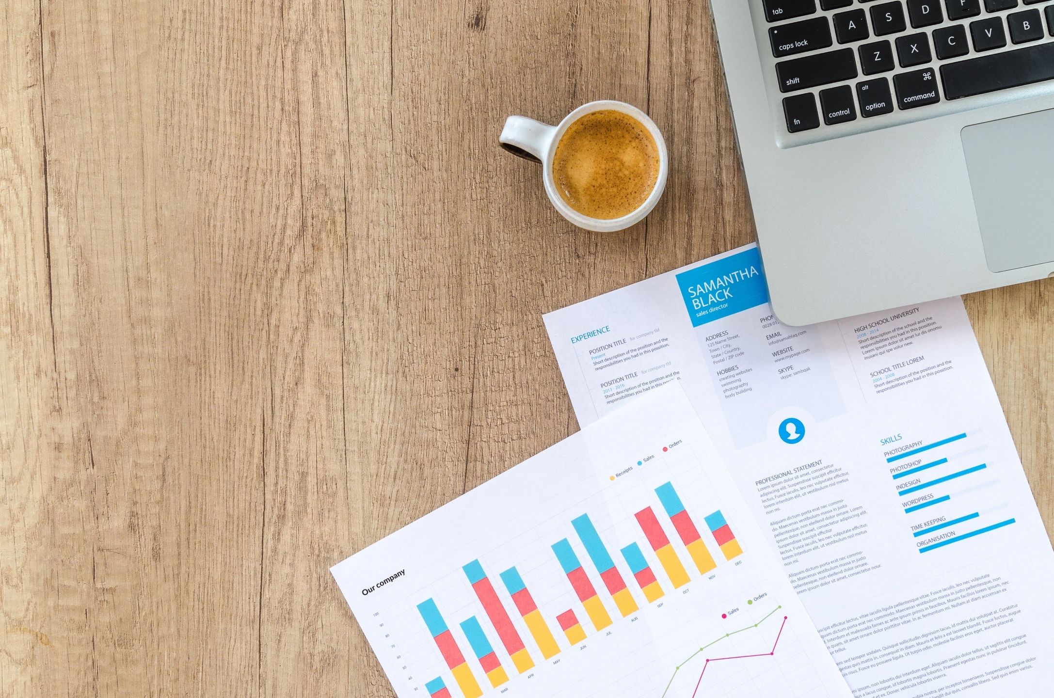 A coffee cup, laptop, and colorful bar charts on a wooden table.